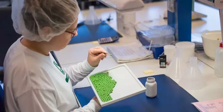 Mitarbeiterin mit Kopfhaube analysiert grüne Tabletten