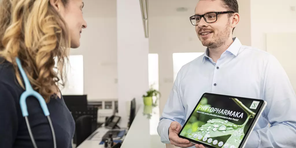 Ein Außendienstmitarbeiter spricht informiert eine Ärztin über pflanzliche Arzneimittel.