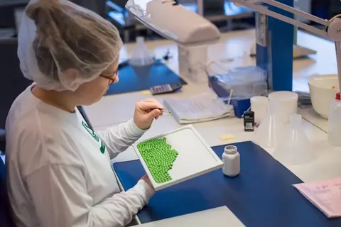 Mitarbeiterin mit Kopfhaube analysiert grüne Tabletten