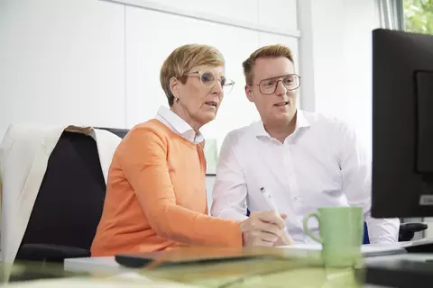Eine Frau und ein Mann sitzen an einem Schreibtisch vor einem Computer