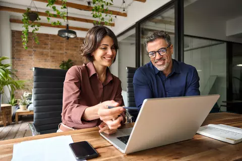 Eine Frau und ein Mann arbeiten vor einem Laptop.