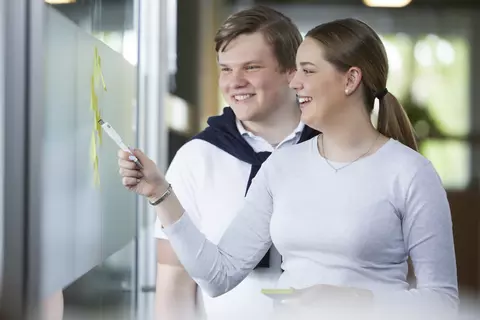 Zwei junge Personen im Austausch an einem Whiteboard